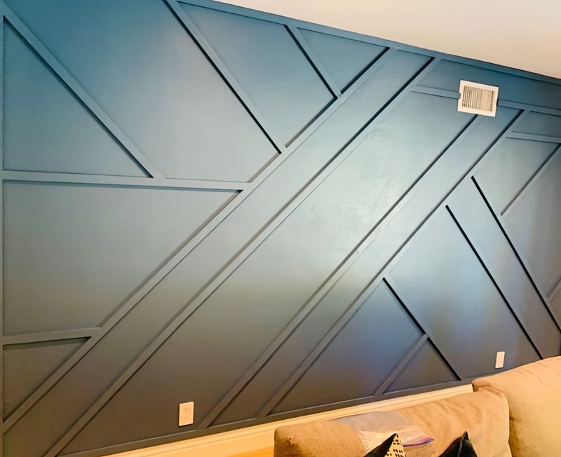 Mavi salon duvarında çapraz kesişen poliüretan duvar çıtası P851350 ile oluşturulmuş modern geometrik dekorasyon.