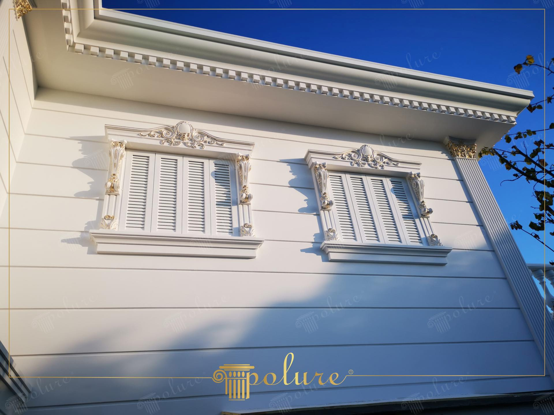 Klasik tarzda süslenmiş iki beyaz pencere, dekoratif poliüretan taçlar, sütunlar ve payandalar ile villa dış cephesi.