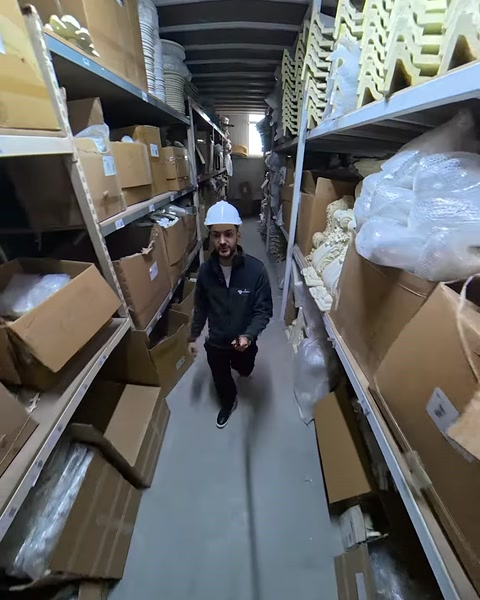 Raflarla çevrili depo koridorunda paketli dekor ürünleri görülüyor.