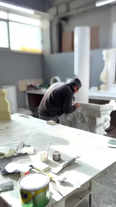 Usta, çalışma tezgâhındaki gri Korint başlığının yüzeyini işliyor.